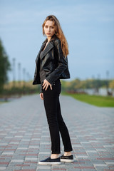 Happy young beautiful woman in black leather jacket black jeans slip-on posing for model tests in the summer park