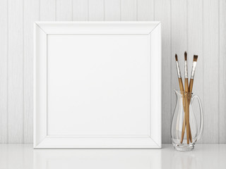 Square interior poster mock up with empty white frame and art brushes on wooden background. 3D rendering.