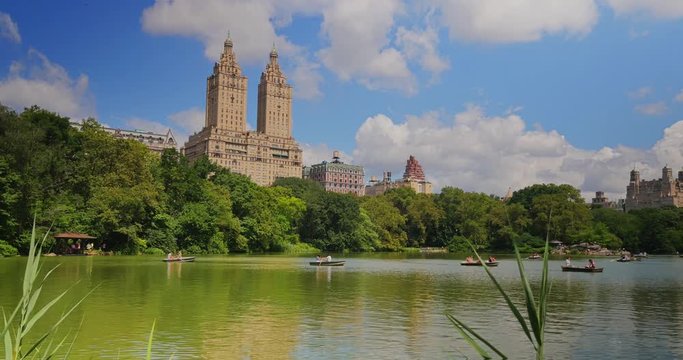 NEW YORK - Circa July, 2016 - A day establishing shot of people in rowboats on the Lake in Central Park with upscale apartment buildings in the distance.  	