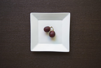 Empty white plate with grapes on wooden table