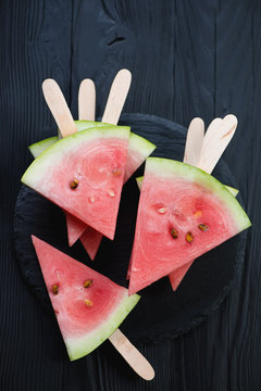 Top view of watermelon slices on sticks, black wooden surface