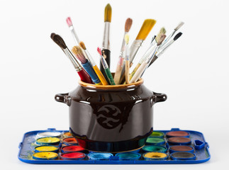 Paint brushes in  clay jug and water paints on white background