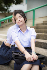 Cute Asian Thai high schoolgirls student couple in school uniform sit and sleep lean on her friend's back on the stairway with a happy smiling face on a building stairs