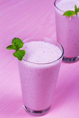 Raspberry milkshake garnished with mint on pink wooden background