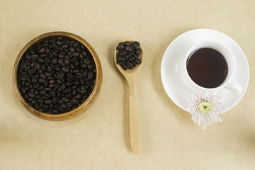 black coffee in white cup with coffee beans in wood plate and spoon. Top view.