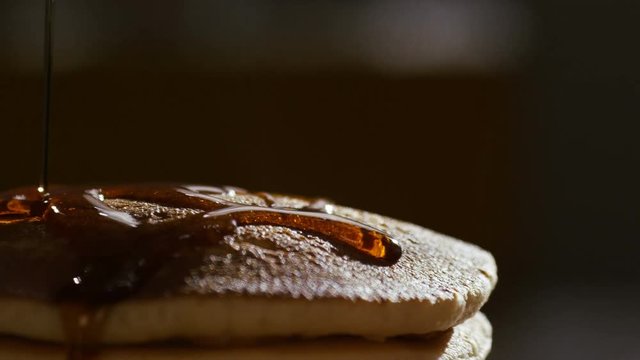 Camera follows maple syrup being poured over hot stacked pancakes and fruit