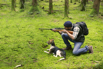 Interracial hunter with his dog in the forest aiming at prey