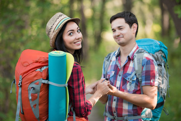 Young Woman and Man with Backpacks in travel style Clothing staying in Forest tenderly holding hands