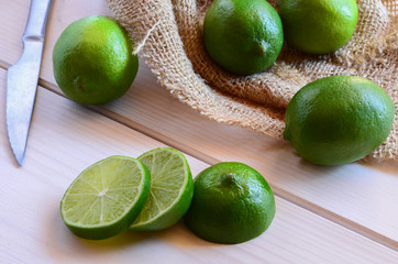 Fresh organic limes on sacking napkin with steel knife on wooden background.
