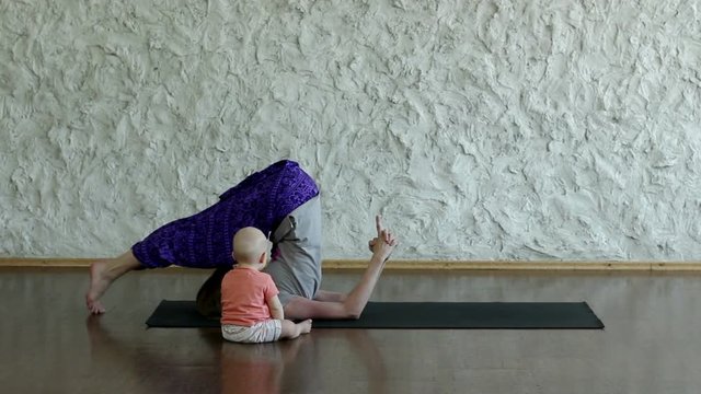 The young blonde girl practicing yoga with her child in the hall. Asana on the balance. The pose of plow. HD