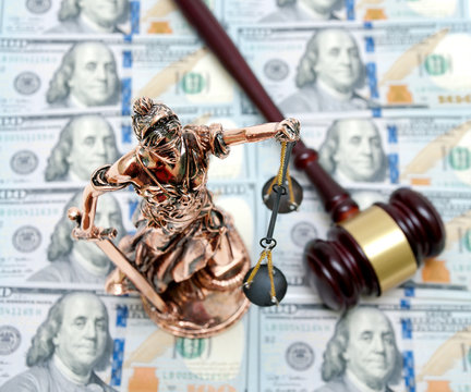 bronze statue of Justice on the background of dollar bills