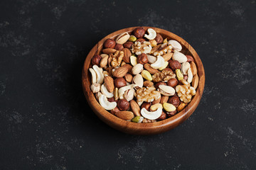 Wooden bowl with mixed nuts on black table from above. Healthy food and snack. Walnut, pistachios, almonds, hazelnuts and cashews.