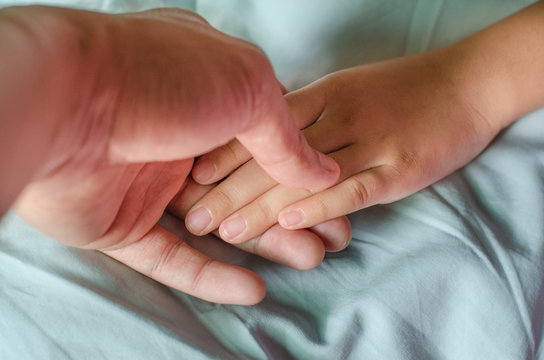 Close-up of a baby hand in father's hand on the blue bed.