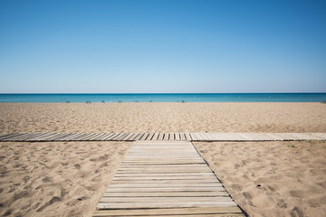 Wooden walkway on the sandy beach of the sea under the blue sky