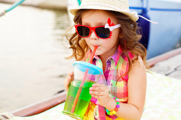 little girl drinking sparkling water on the pier