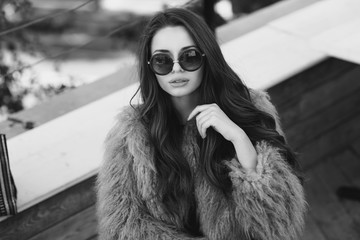 Trendy drssed fashionable girl wearing fur coat. Young pretty beautiful woman with long curly hair looking at you.