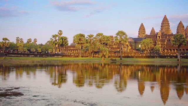 1920x1080 video - Afternoon sun bathes the ancient architecture of Angkor Wat in golden hues. Palm trees dot the foreground and the five towers reach skyward in the background