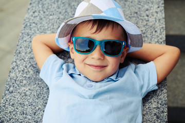 Close-up of small boy in sunglasses lying with hands under his h