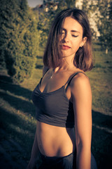 Obraz premium Young sexy woman in a short top and leggins with beautiful modern make-up and hair dancing in a park,