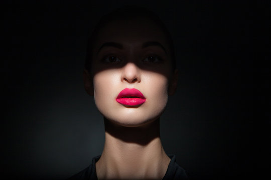 Beautiful model with bright pink lips and face half covered in shadow