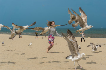 Happy girl trying to fly with birds on the beach