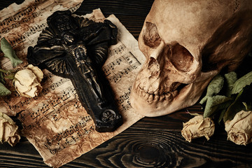 Vintage still life with skull, crucifix, dry roses and music not