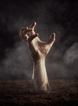 Hand of zombie in dirt climbs out of the ground
