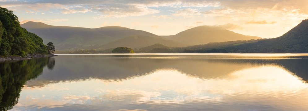 Golden Sunlight Shining Through Mountains On Peaceful Calm Morning At Derwentwater, Lake District, UK.