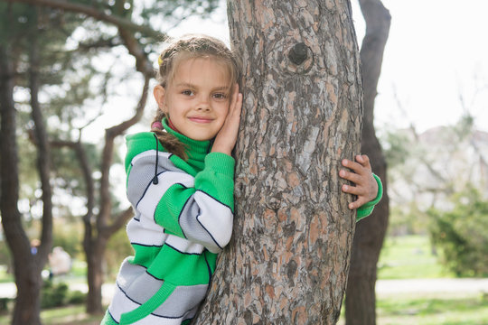 Joyful seven-year old girl sitting on a tree trunk in the early spring