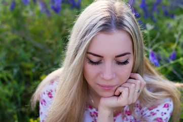 Portrait of a young blond female sitting near grass with eyes shut