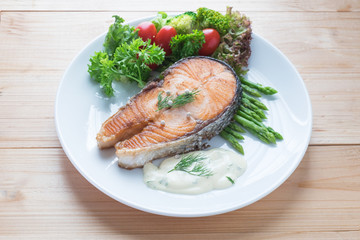 Fried salmon with vegetable on a round white plate on wooden bac