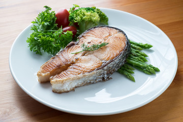 Fried salmon with vegetable on a round white plate on wooden bac
