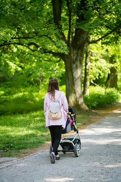 Happy mother walking with baby stroller in park