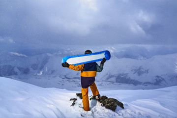 Snowboarder is turned back over  cliff snowy weather in  mountains.