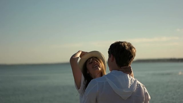 Couple hugging and girl play with hat on sea background.