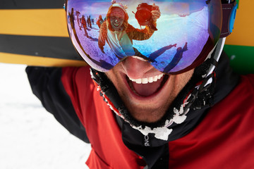 Happy snowboarder in mask with friend taking shot in reflection