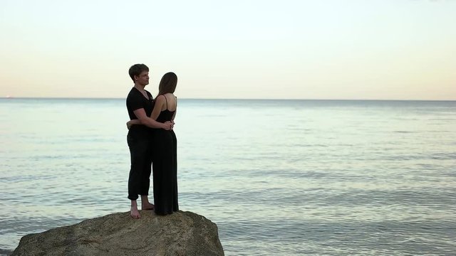 Couple in black clothing embracing on the rock by the sea.