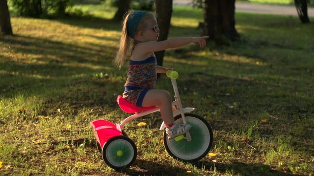 A little girl rides in the evening on a pink tricycle through the city Park
