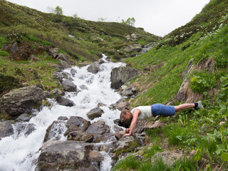 Young woman in shorts does exercises on the bank of a stream on a grass background with stones
