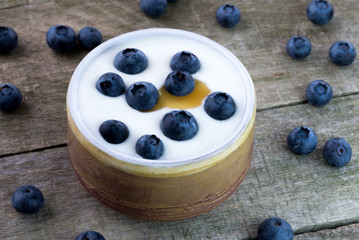 White yogurt with whole blueberries and honey on natural rustic wooden table.
