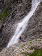 Woman with backpack standing on the edge of a cliff with outstretched hands up against the background of a huge waterfa