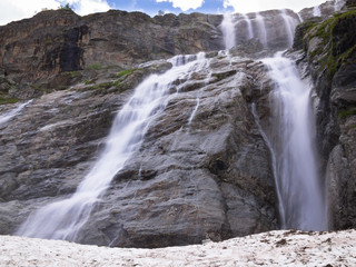 Panorama of a large stepped waterfall with snow on the background of sky with clouds