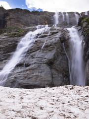 Toned image panorama of a large stepped waterfall with snow on the background of sky with clouds