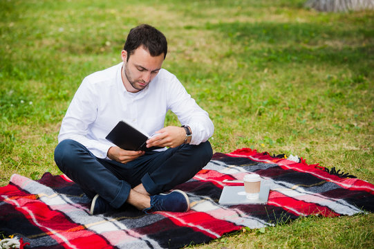handsome young businessman reading book lying in the park