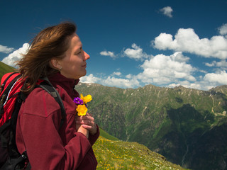 Woman closeup holding a bouquet of flowers on a background of high mountains and sky with clouds