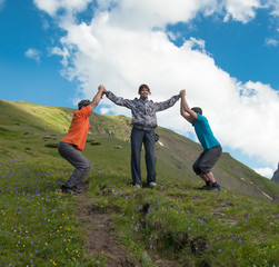 Young woman holding hands with two laughing man on a background of mountains and cloudy sky