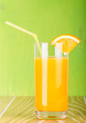 Orange juice glass with slice on green background