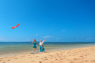 Happy family on beach - grandmother, mother and baby girl have fun. Woman run with water splashes along sea surf and launch bird kite. Active parent, people activity on summer vacation with children