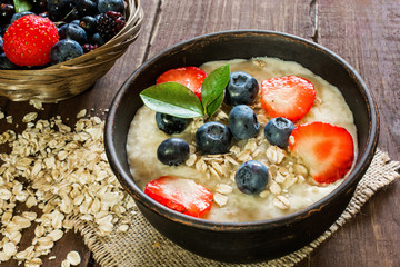 Oatmeal porridge in brown pottery bowl with ripe berries. healthy breakfast