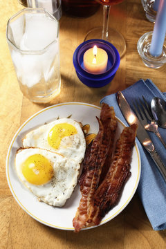 Bacon, eggs and water by candle light suggests breakfast for dinner